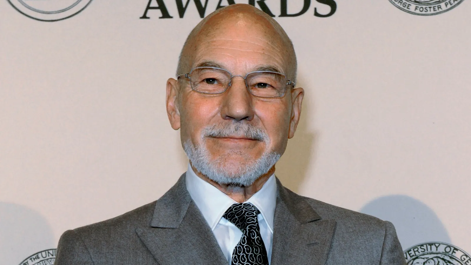 Patrick Stewart smiling in a grey suit and glasses at a Peabody Awards event